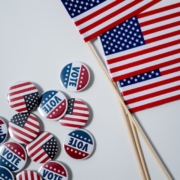 Photo of American flag and vote sticker. Photo by cottonbro: https://www.pexels.com/photo/american-flags-and-pins-on-white-background-4669109/